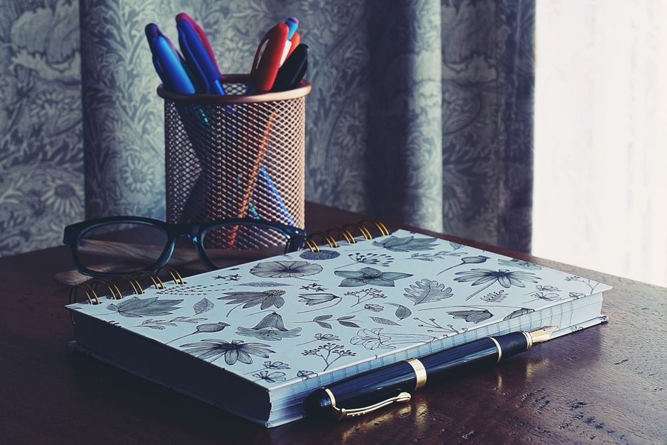A stylish workspace featuring a floral notebook, glasses, and pens on a wooden desk.